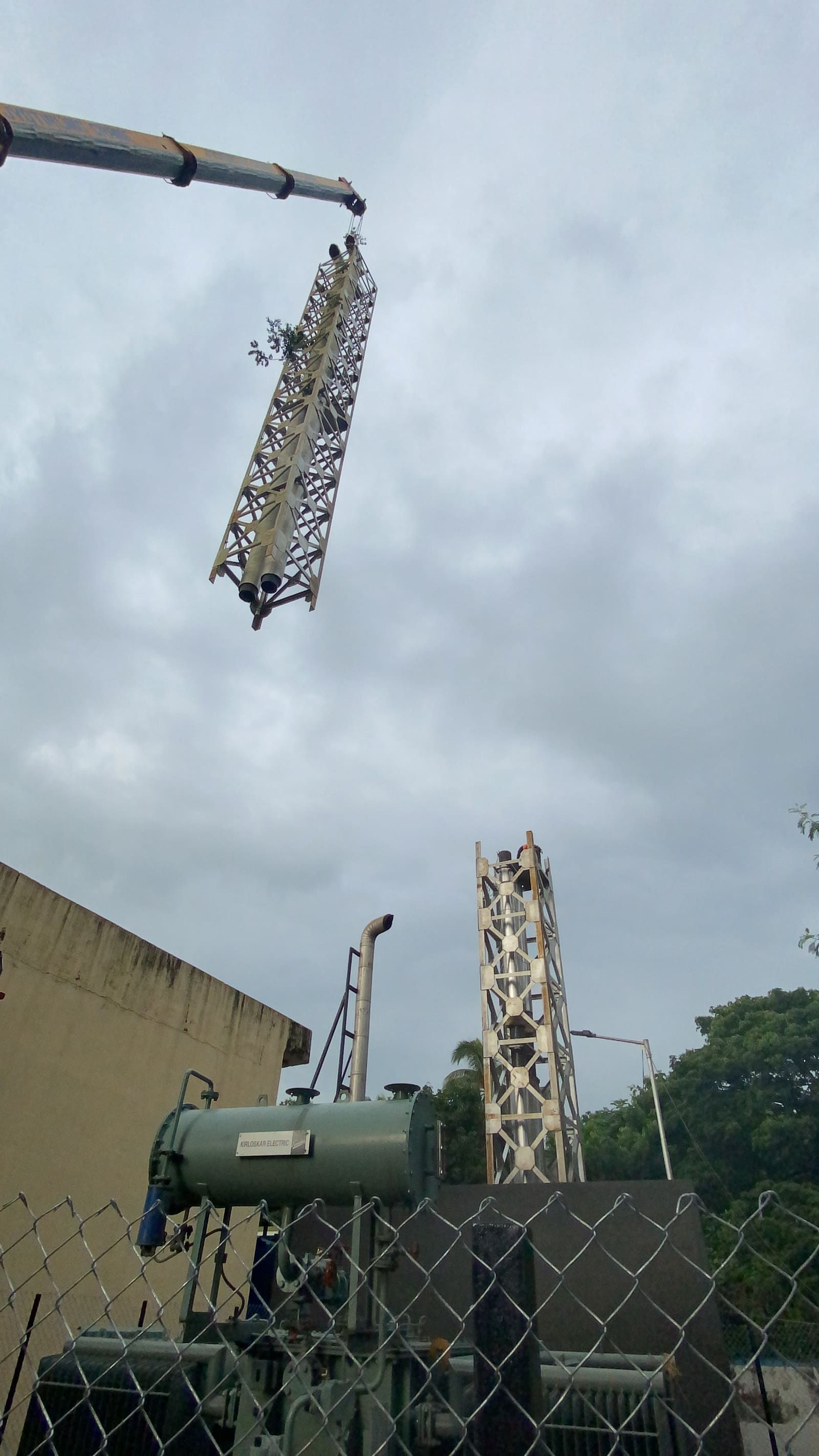 Twin-flue lattice stack section suspended mid-air by crane above the standing base section