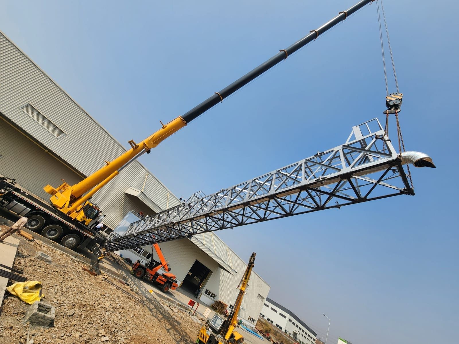 Telescopic crane lifting the complete lattice column off the ground, rain-cap elbow at its head