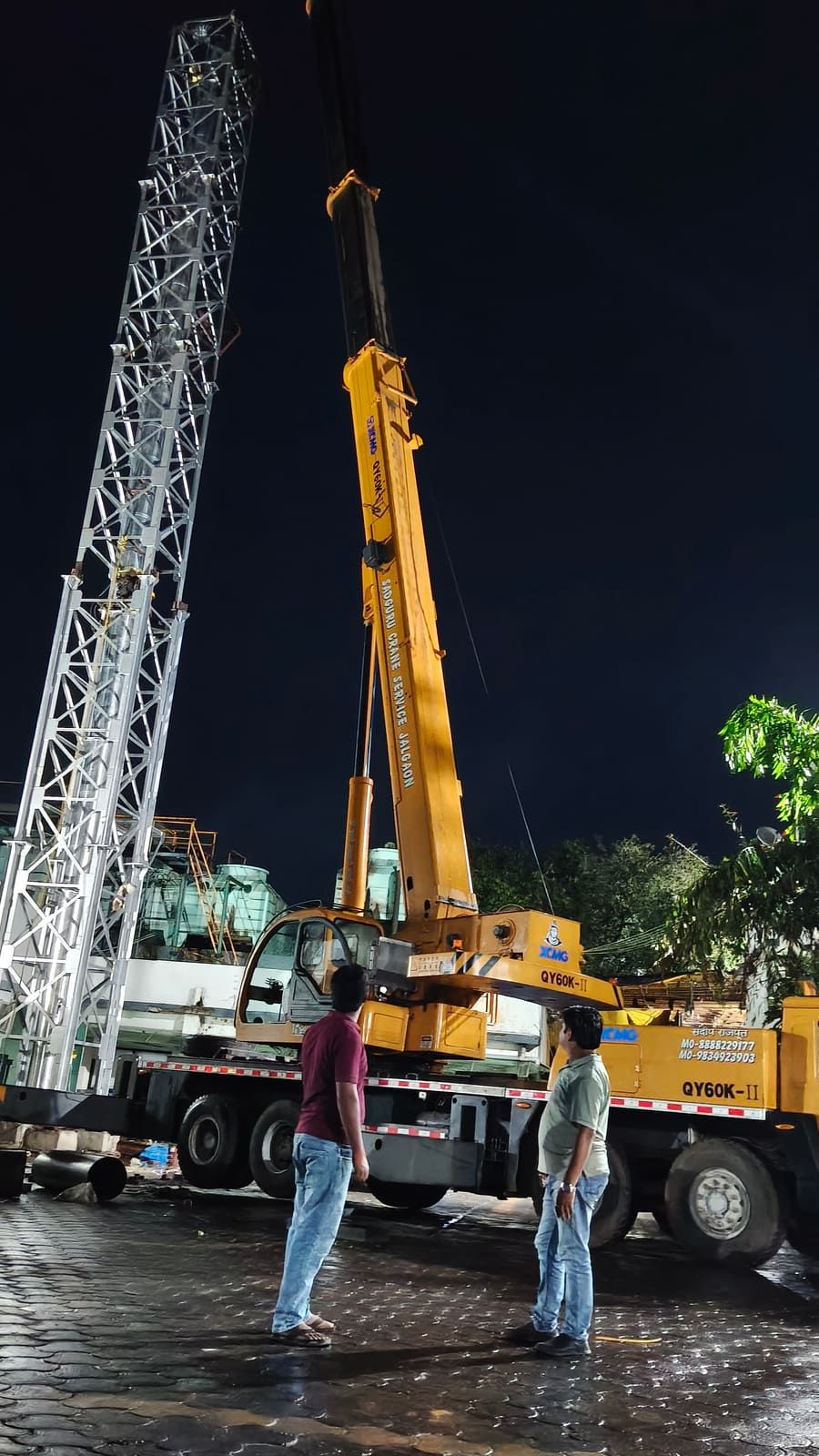 Two engineers watching a crane hold a lattice stack section during a night lift