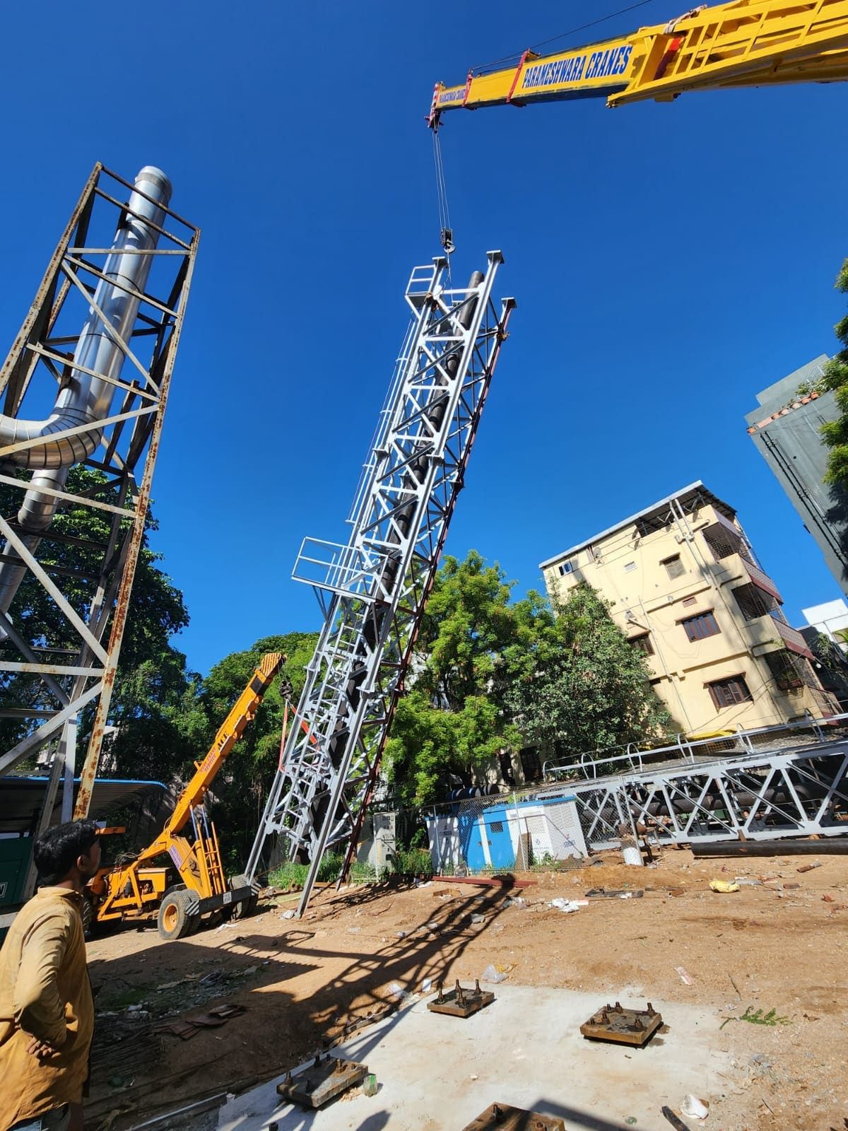 Crane lifting a galvanised lattice stack section over anchor-bolt foundations