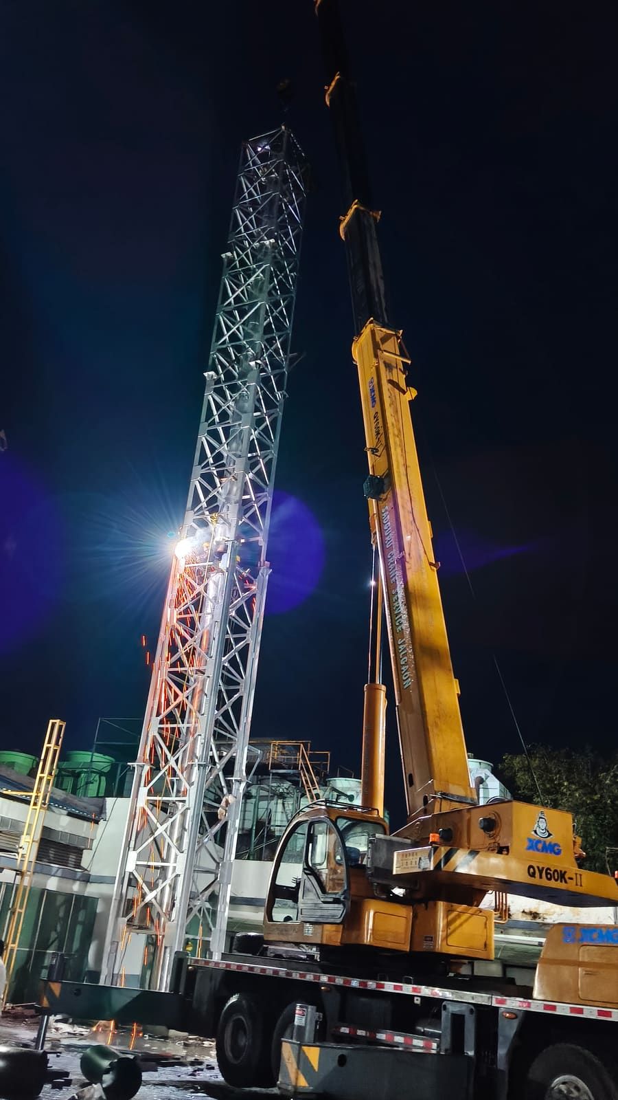 Night crane erection of a self-supporting lattice chimney tower beside plant buildings