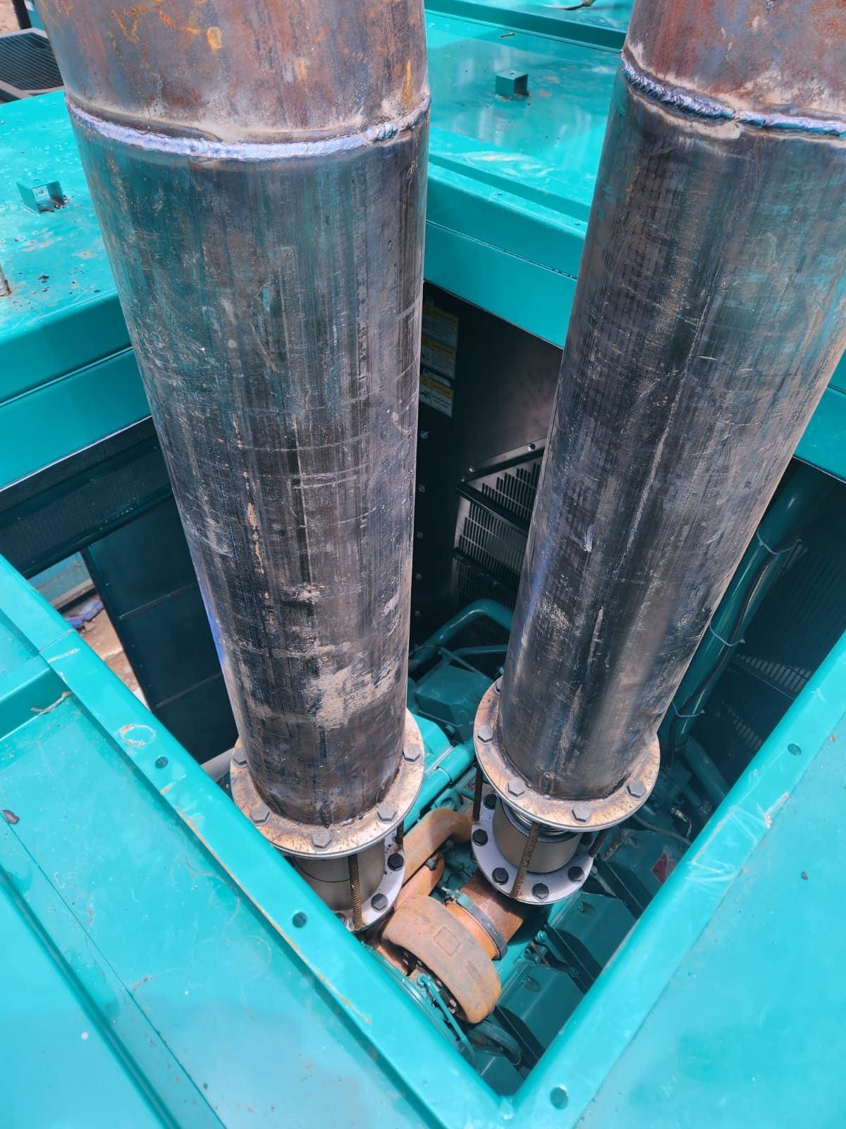 Twin exhaust risers with flanged expansion bellows rising from a DG enclosure roof